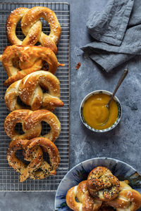 An assortment of baked pretzels served with mustard against a dark background.