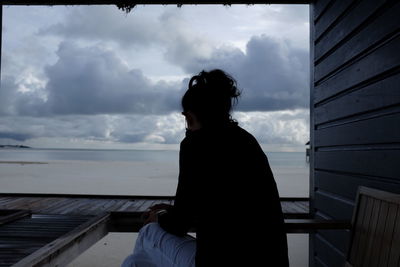 Man looking at sea against cloudy sky