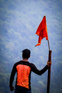 Rear view of man holding umbrella against sky