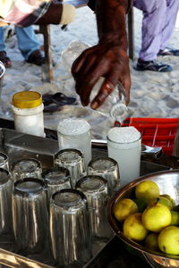 Cropped hand pouring lemon juice in glass at sandy beach