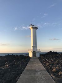 Lighthouse by sea against sky during sunset