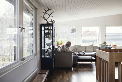 Full length of senior man sitting on sofa in living room at home