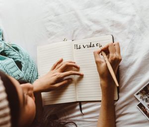 Directly above shot of woman writing on book in bedroom
