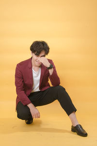 Full length of young man looking away while sitting on orange sunset