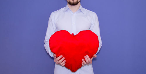 Midsection of man with red heart shape against gray background