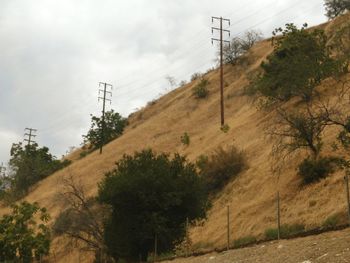 Low angle view of electricity pylon against cloudy sky