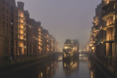 Canal amidst buildings in city at night