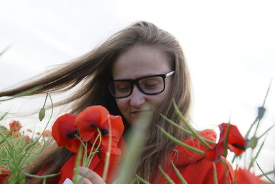 Low angle view of beautiful woman holding fresh red poppy flowers against sky