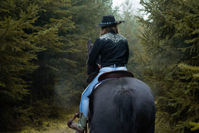 Rear view of woman riding horse in forest