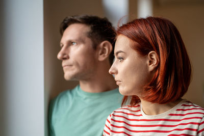 Unsmiling man and woman look out window. disappointed, cloudy cold weather outside close up portrait