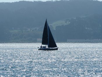 Sailboat sailing on sea against mountains