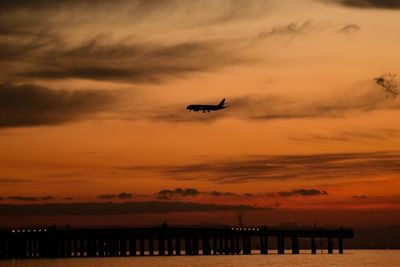 Silhouette airplane flying over sea against sky during sunset