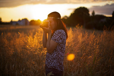 Side view of woman photographing while standing on grassy field