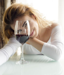 Portrait of young woman with blond hair by wineglass at home