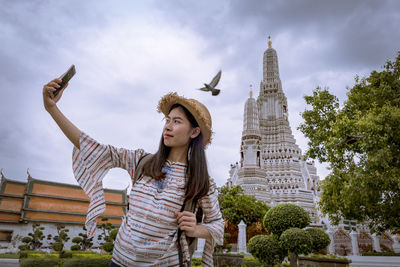 Low angle view of young woman standing against sky