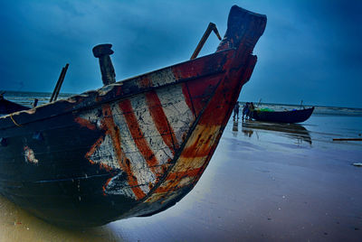 Abandoned boat moored at beach against sky