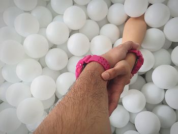 Cropped image of couple holding hands amidst white balloons