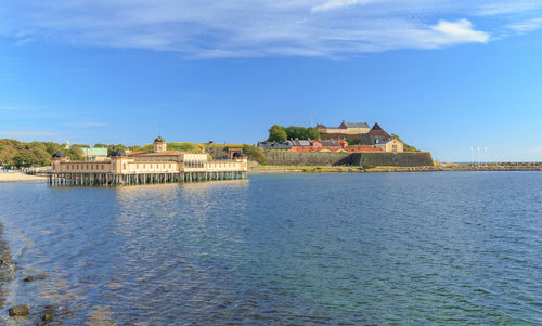 Buildings by river against blue sky