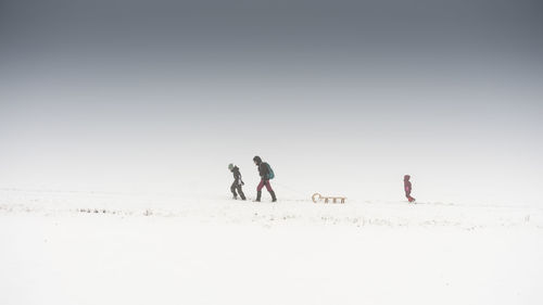 Family with sled on snow covered field against sky