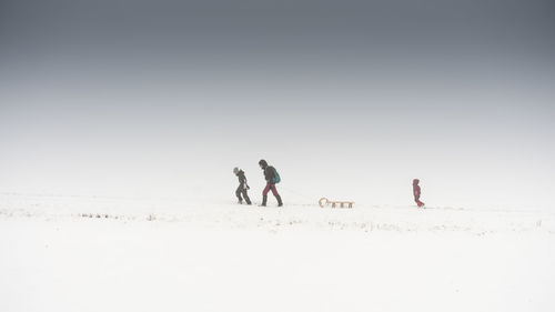 People walking on snow field against clear sky