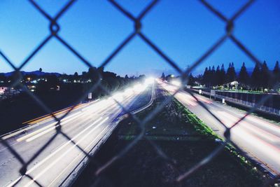 Light trails on chainlink fence against clear sky at night