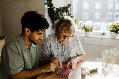 Male nurse explaining medication dosage to senior woman sitting at home