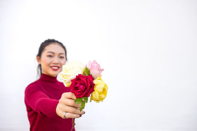 Portrait of smiling woman holding flower against white background
