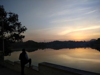 Rear view of silhouette man sitting against sky during sunset