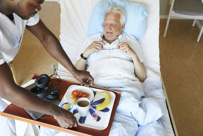 High angle view of male nurse serving breakfast to senior man in hospital ward