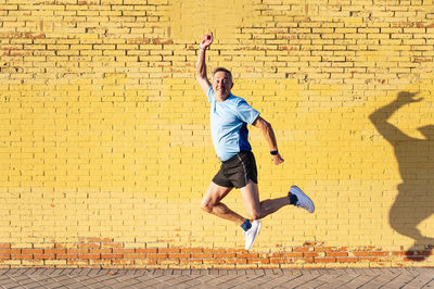 Full length of man jumping against brick wall