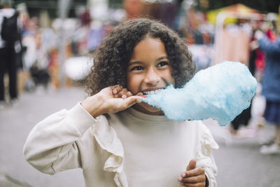 Thoughtful girl eating blue cotton candy at amusement park