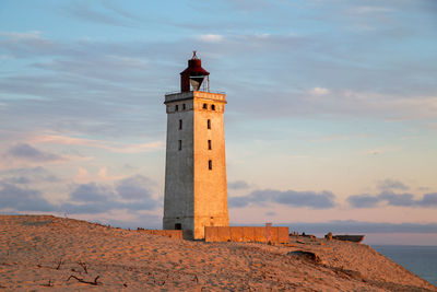 Lighthouse by sea against sky during sunset