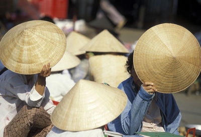 Vendors hiding face while holding asian style conical hats at market