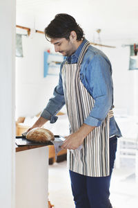 Side view of man holding freshly baked bread in tray at home