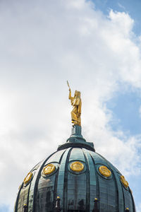 Low angle view of statue on dome against cloudy sky