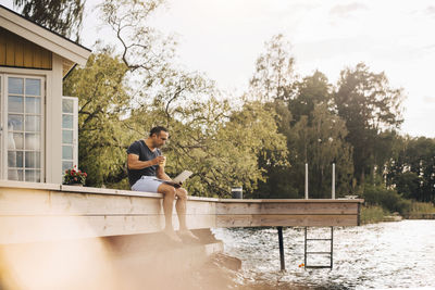 Mature man having juice while using laptop on patio by lake