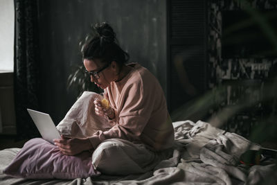 Woman using mobile phone while sitting on bed at home