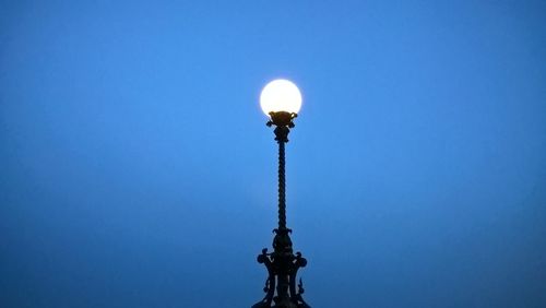 Low angle view of illuminated light bulb against blue sky