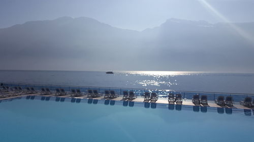 Empty deck chairs at poolside by sea against mountains