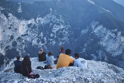 People sitting on rock by snowcapped mountain