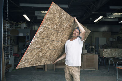 Carpenter carrying wooden plank at workshop