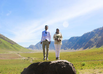 Couple jumping on rock at landscape against sky