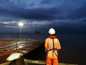 Rear view of man standing at sea against sky