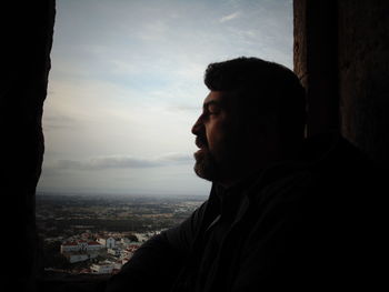 Side view of man looking away by window against sky