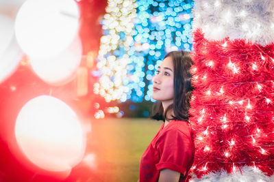 Young woman looking away standing against illuminated lights at night