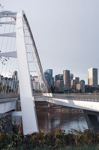 Bridge over river by buildings against clear sky