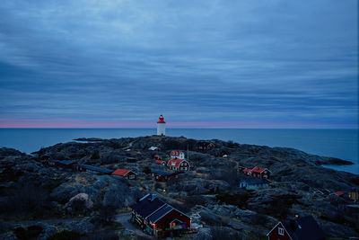 Lighthouse by sea against sky at sunset