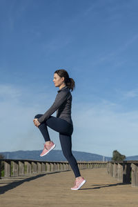  woman doing running warm-up, hamstring muscles stretch standing wtih single knee to chest stretch. 