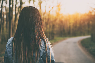 Rear view of woman standing on road in forest during sunset