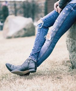 Low section of woman sitting on rock over field